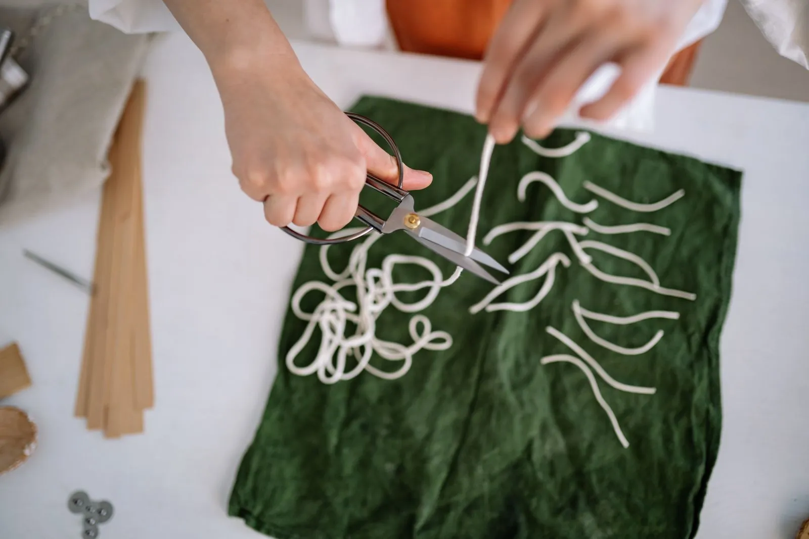 Close-up of hands cutting candle wicks on green fabric, showcasing craft skills.